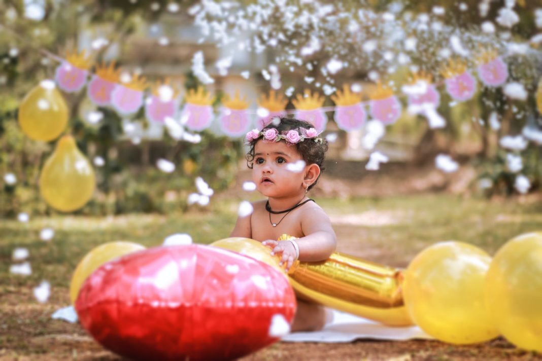 photograph of a baby with a flower crown holding balloons